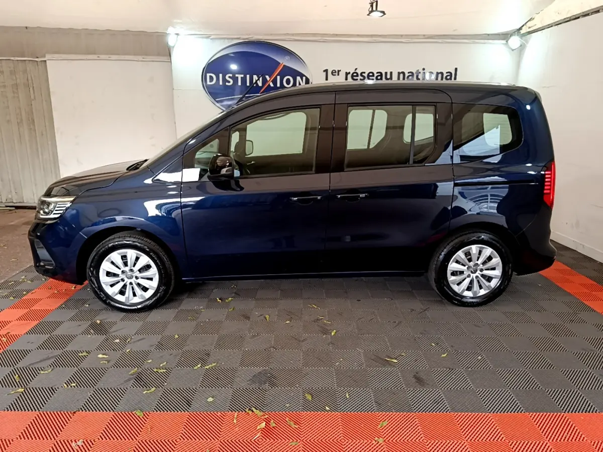 Profil latéral gauche d'un Renault Kangoo bleu 2023 dans un showroom avec jantes argentées et vitres teintées.