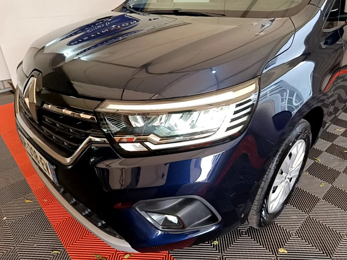 Vue 3/4 avant droit d'un Renault Kangoo bleu 2023 avec phares LED et calandre chromée visible.