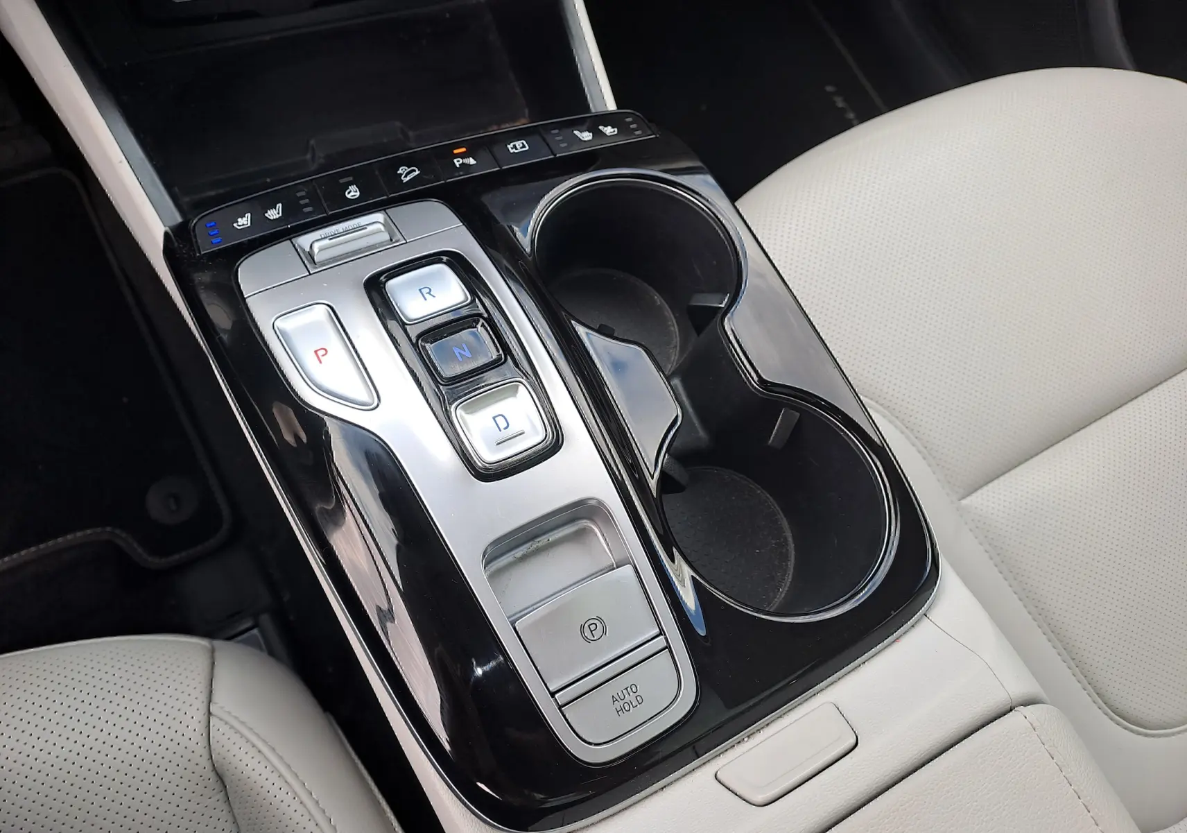 Vue rapprochée de la console centrale noire brillante avec commandes de boîte auto et sièges beige clair du Hyundai Tucson 2023.