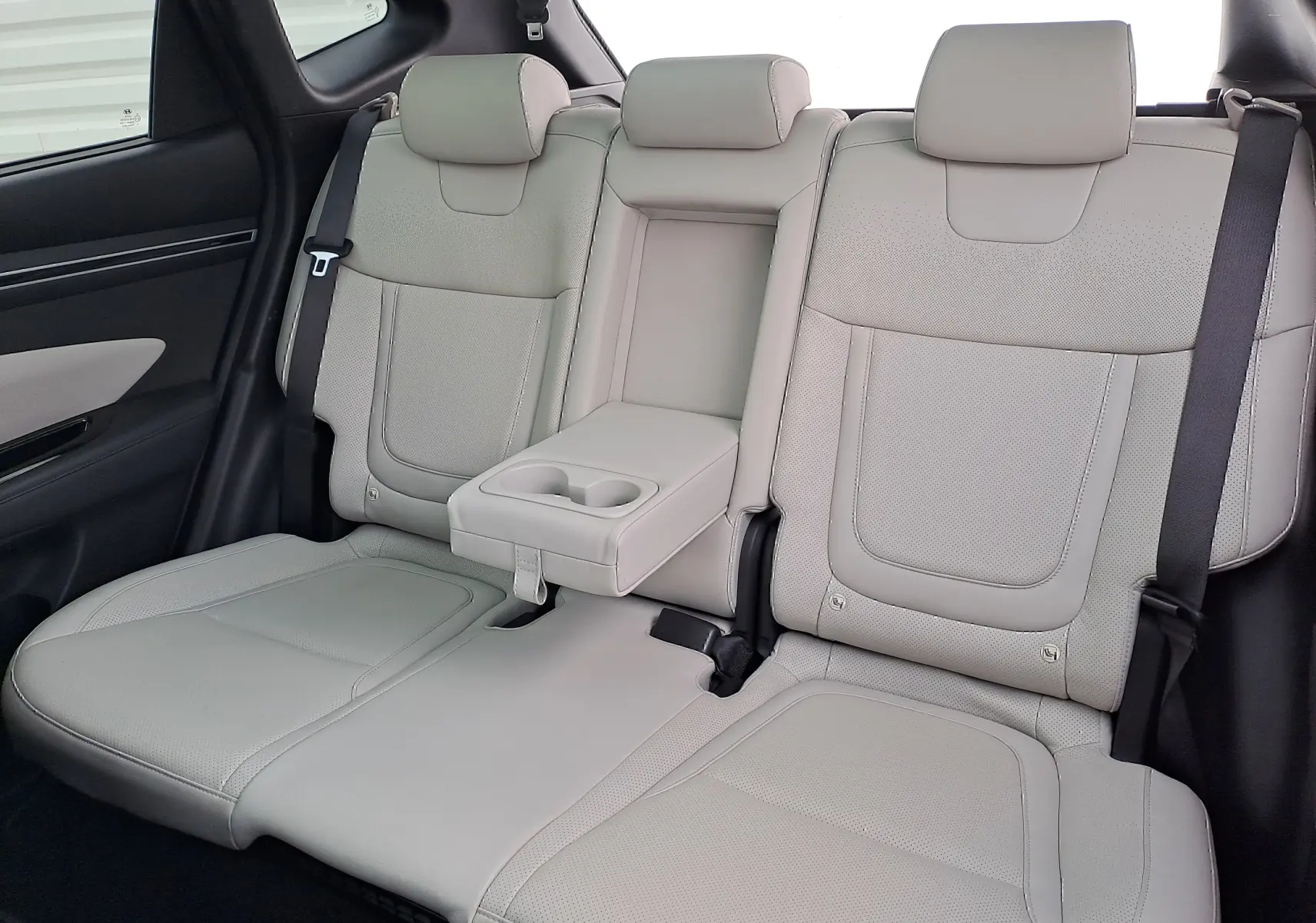 Vue rapprochée des sièges arrière en cuir beige du Hyundai Tucson 2023, avec accoudoir central et porte-gobelets intégrés.