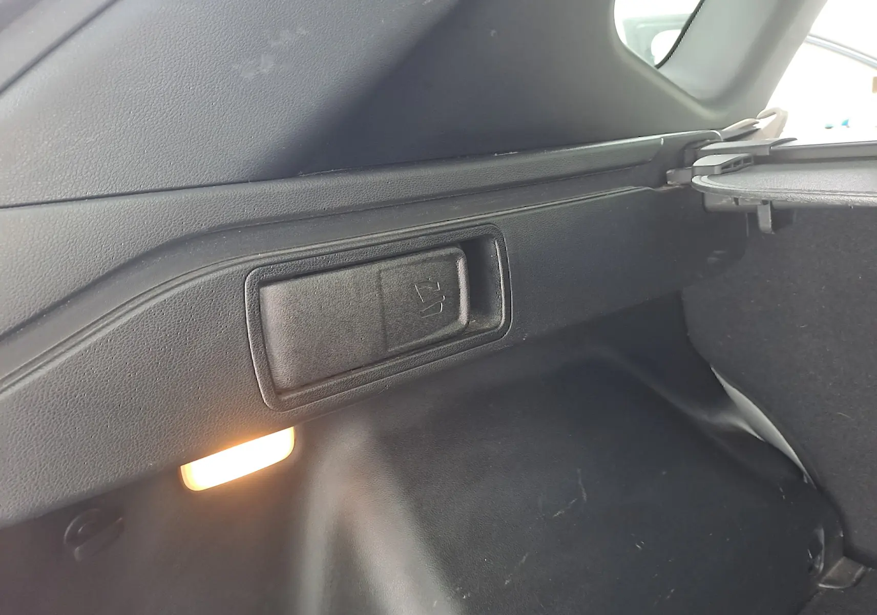 Détail intérieur du coffre du Hyundai Tucson 2023, côté droit, avec éclairage et poignée de rabattement des sièges.