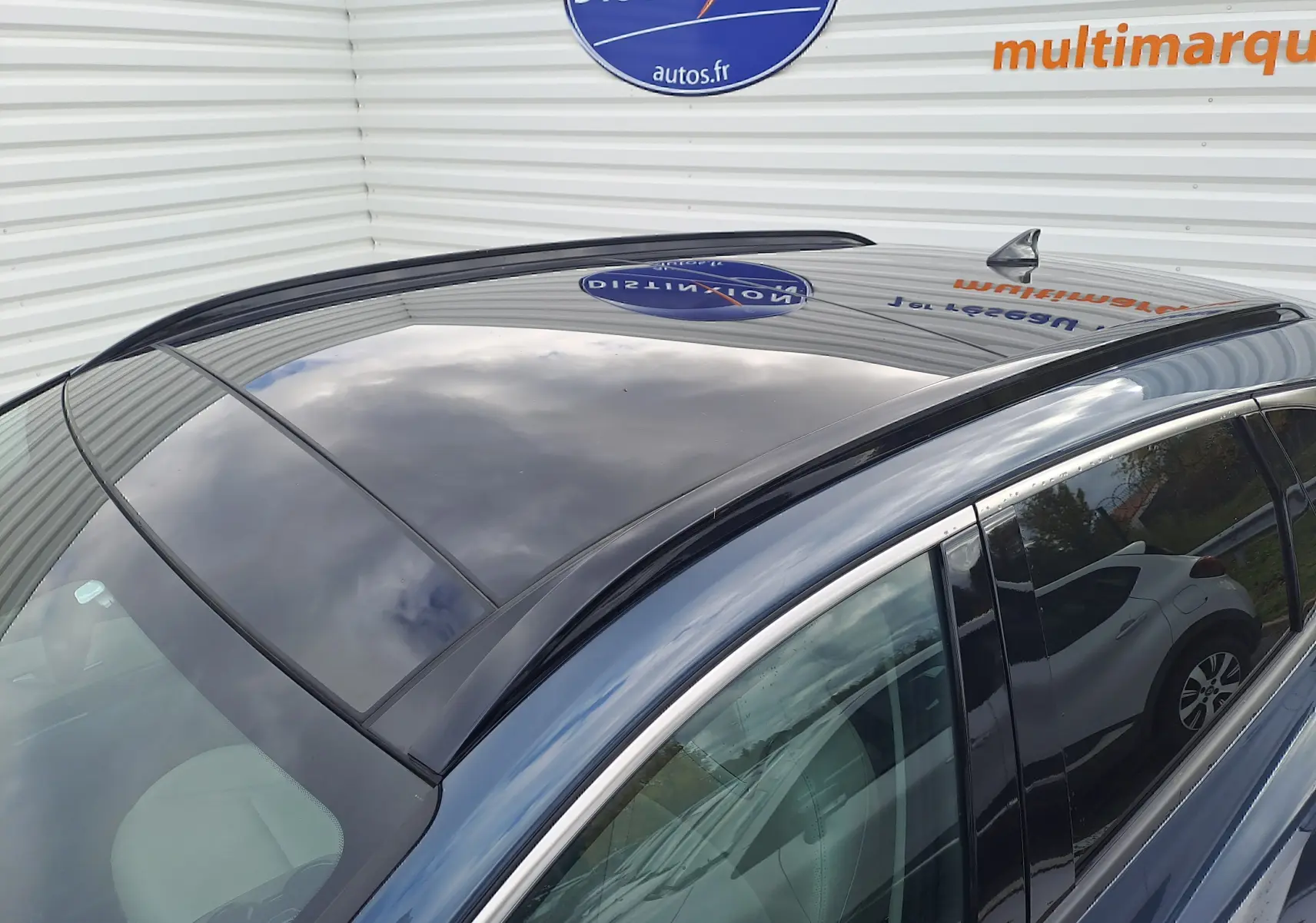 Toit panoramique en verre noir du Hyundai Tucson Cypress Green vu de dessus côté droit, reflet du ciel et panneau mural visible.