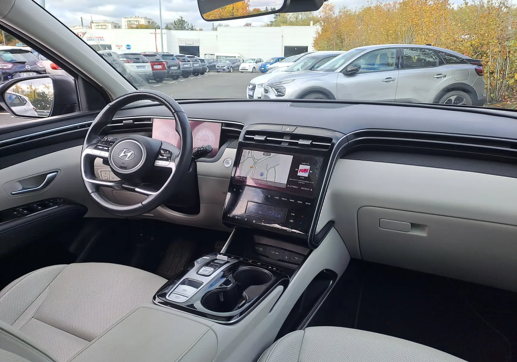Intérieur beige clair du Hyundai Tucson 2023, vue depuis le siège conducteur sur le tableau de bord et écran tactile central.