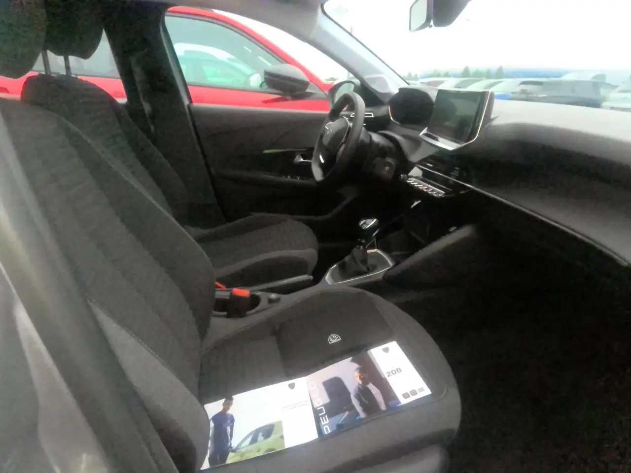 Vue intérieure côté conducteur de la Peugeot 208 gris clair 2024 avec tableau de bord et écran tactile central.
