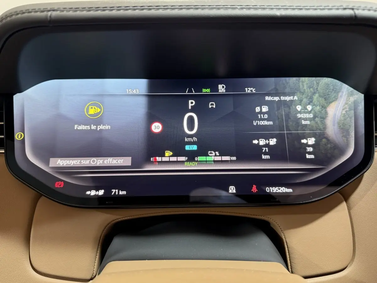 Tableau de bord numérique du Range Rover PHEV 2024 affichant vitesse, autonomie et alertes, vue frontale rapprochée.