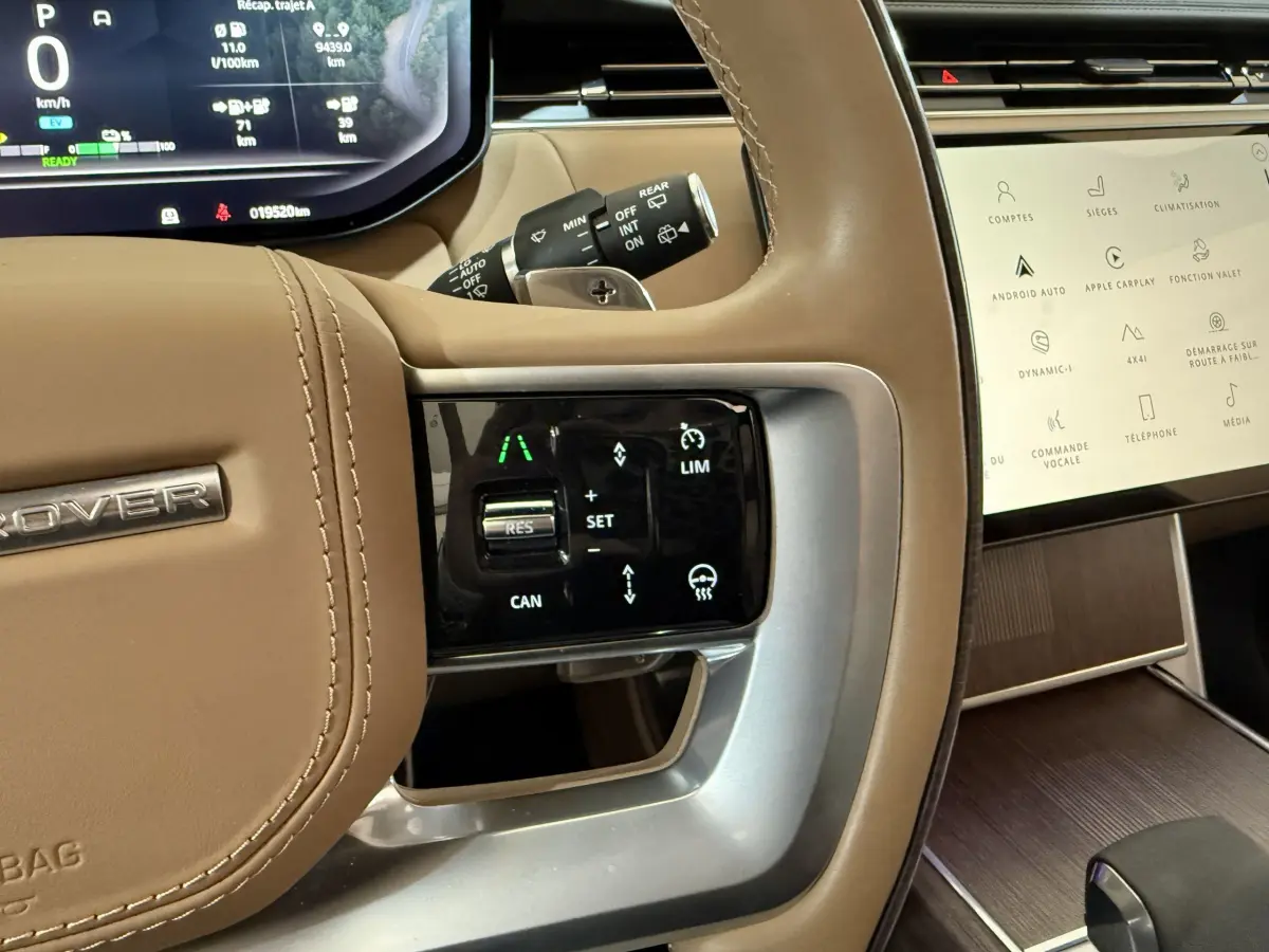 Gros plan sur le volant beige du Range Rover PHEV 2024 avec commandes tactiles et tableau de bord digital.