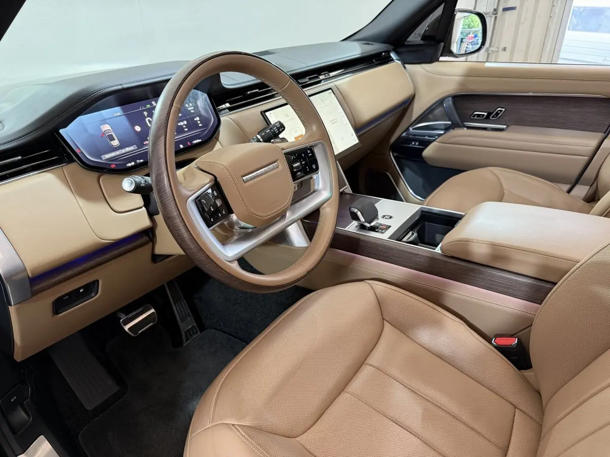 Intérieur beige du Range Rover PHEV 2024 vu côté conducteur, avec tableau de bord digital et volant cuir bois.