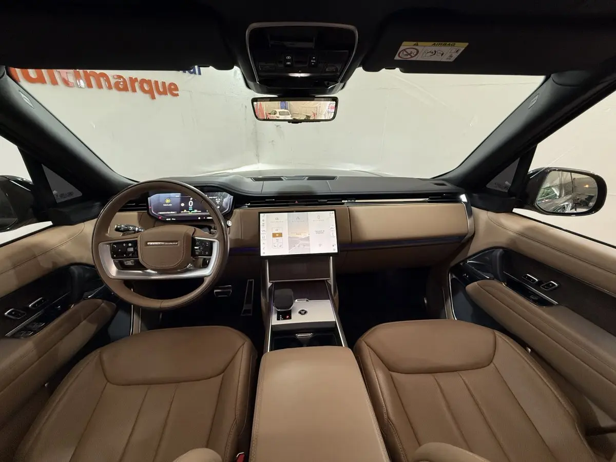 Vue intérieure avant du Range Rover PHEV 2024 avec tableau de bord beige, écran tactile central et volant cuir bois.
