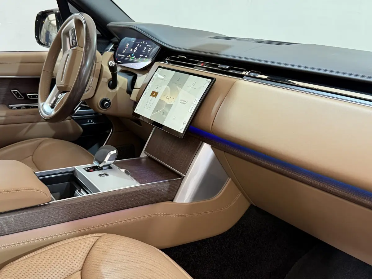 Vue intérieure côté passager du tableau de bord beige et bois du Range Rover PHEV P550e 2024 avec écran tactile central.