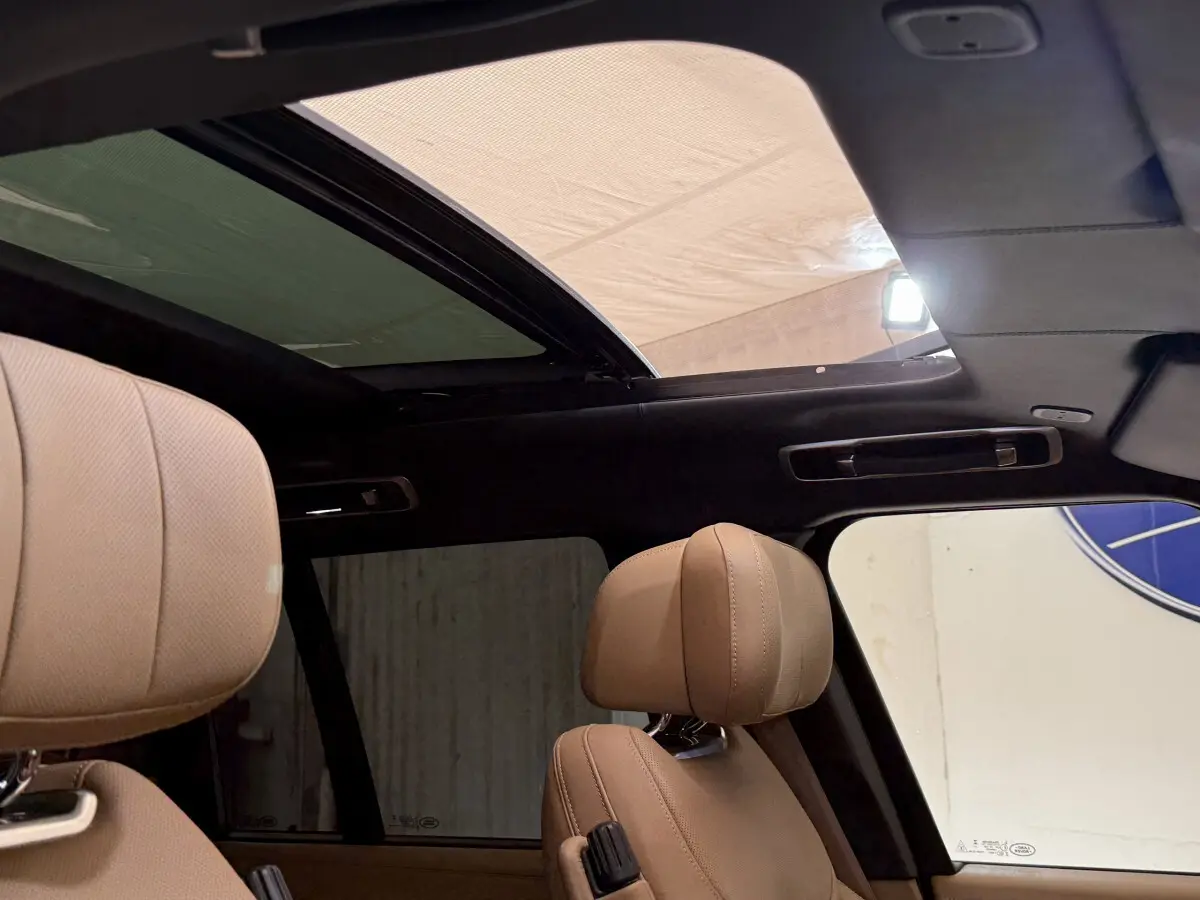 Vue intérieure du toit ouvrant panoramique et des appuie-têtes en cuir beige du Range Rover noir 2024.