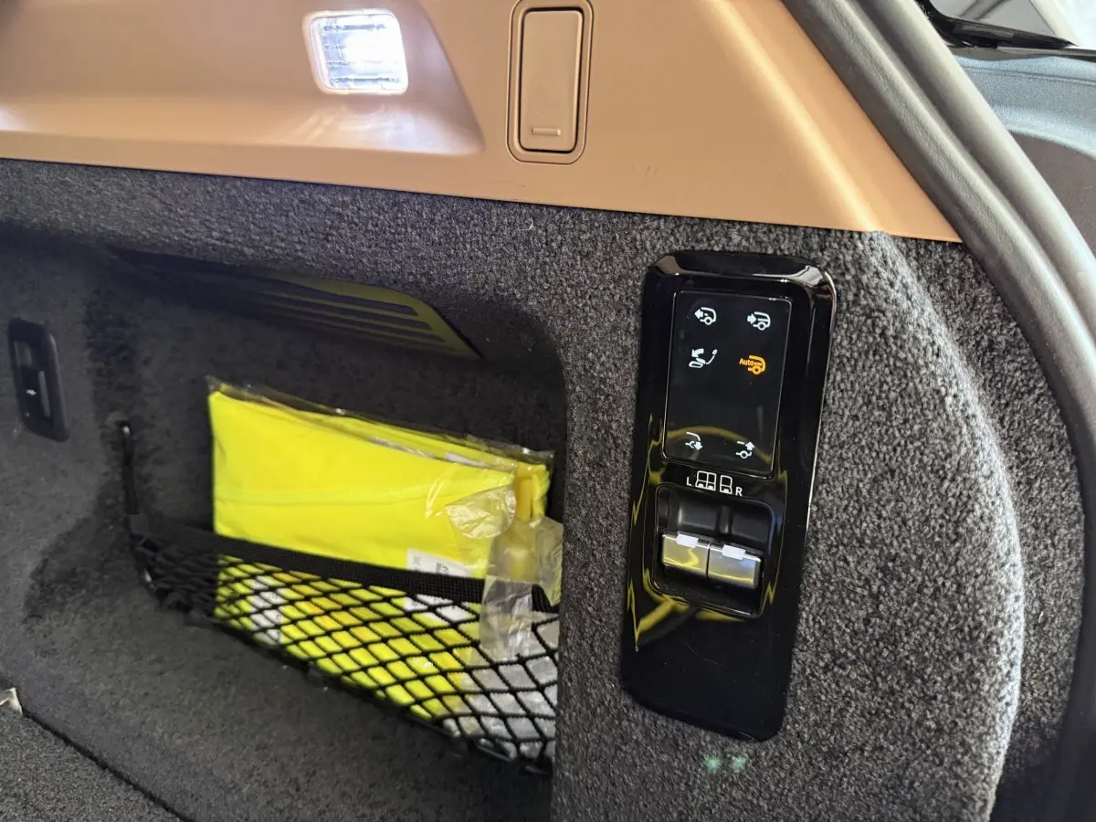 Détail du coffre du Range Rover PHEV noir 2024 montrant les commandes électriques et un gilet jaune rangé dans un filet.