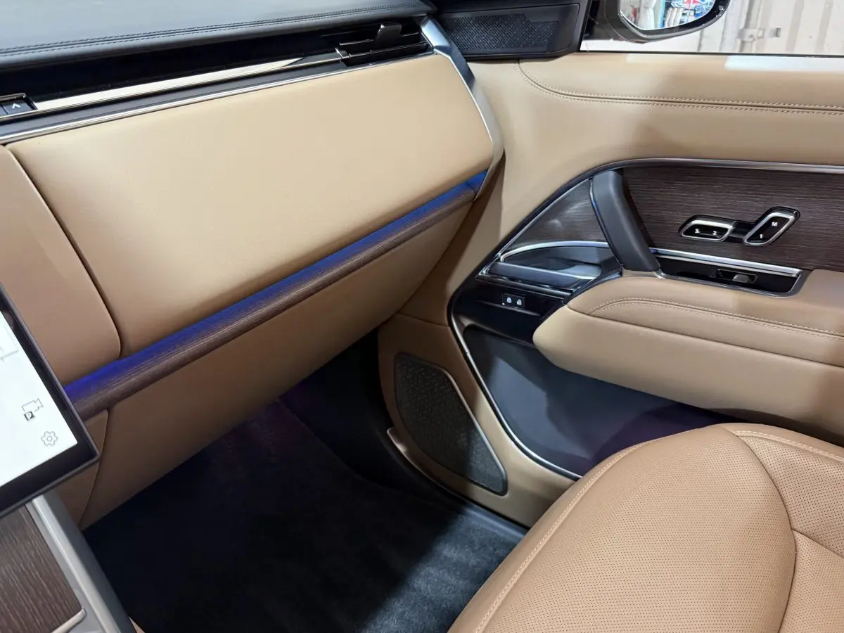 Intérieur côté passager du Range Rover PHEV noir 2024, avec sellerie beige et inserts bois sur la porte.