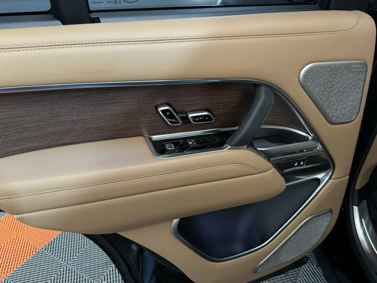 Gros plan sur la porte intérieure côté gauche du Range Rover PHEV 2024, cuir beige et inserts bois avec commandes électriques.