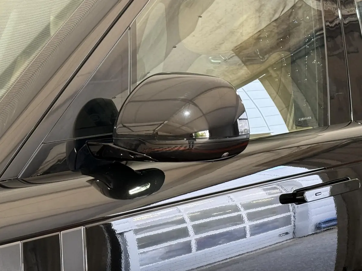 Gros plan sur le rétroviseur rabattable électrique côté gauche d’un Range Rover PHEV noir brillant.