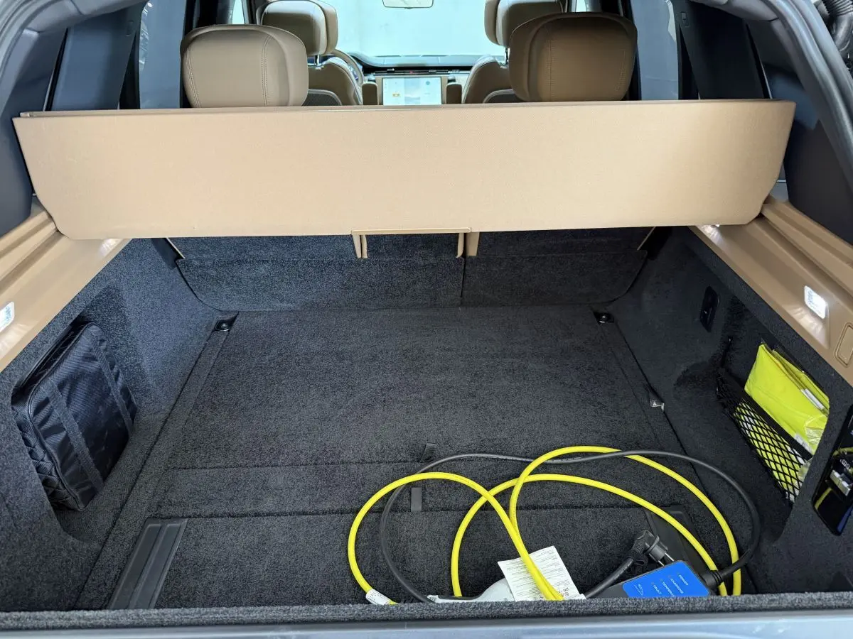 Coffre ouvert d’un Range Rover PHEV noir, vue arrière montrant la moquette noire et un câble de recharge jaune.