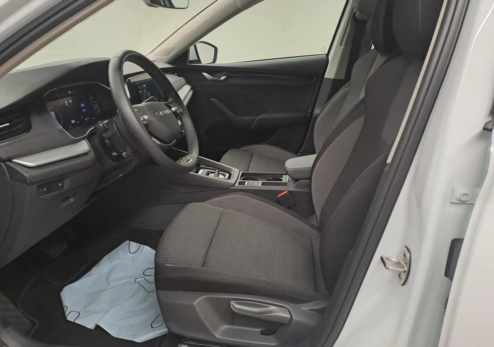 Vue intérieure côté conducteur de la Skoda Octavia Combi blanc Moon 2025 avec sièges tissu gris et volant cuir noir.