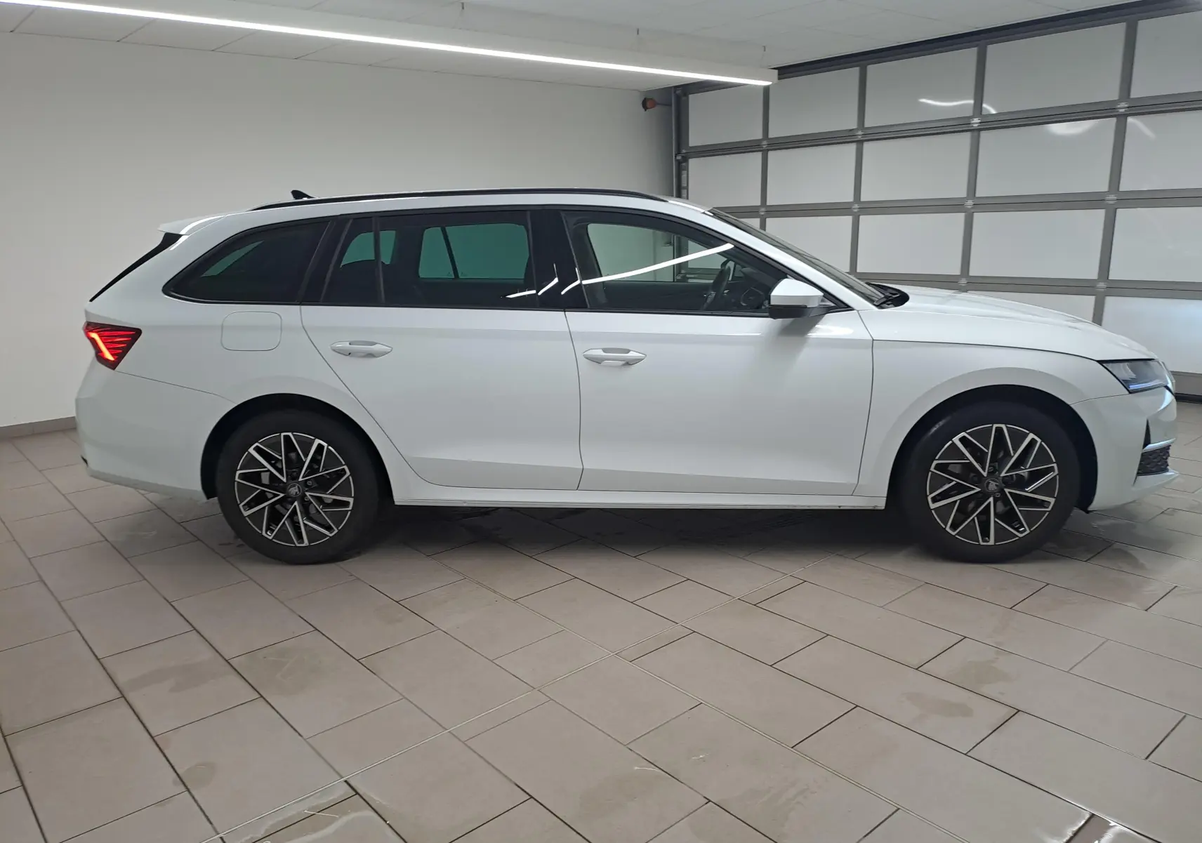 Vue de profil droit d’une Skoda Octavia Combi 2025 blanche Moon avec jantes alliage noires polies dans un garage.