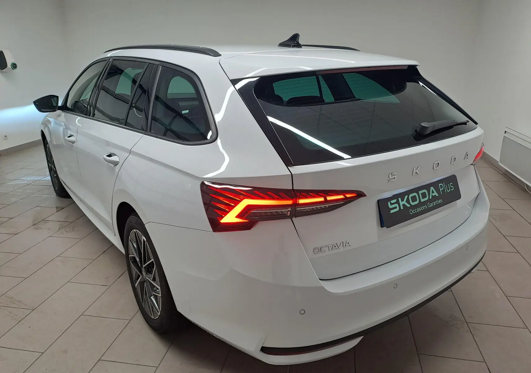 Vue 3/4 arrière droite d'une Skoda Octavia Combi blanche Moon avec feux arrière allumés et jantes alliage 17'' noires polies.