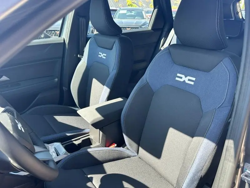 Vue intérieure rapprochée des sièges avant bleu et noir du Dacia Bigster 2025 avec accoudoir central et logo DC brodé.