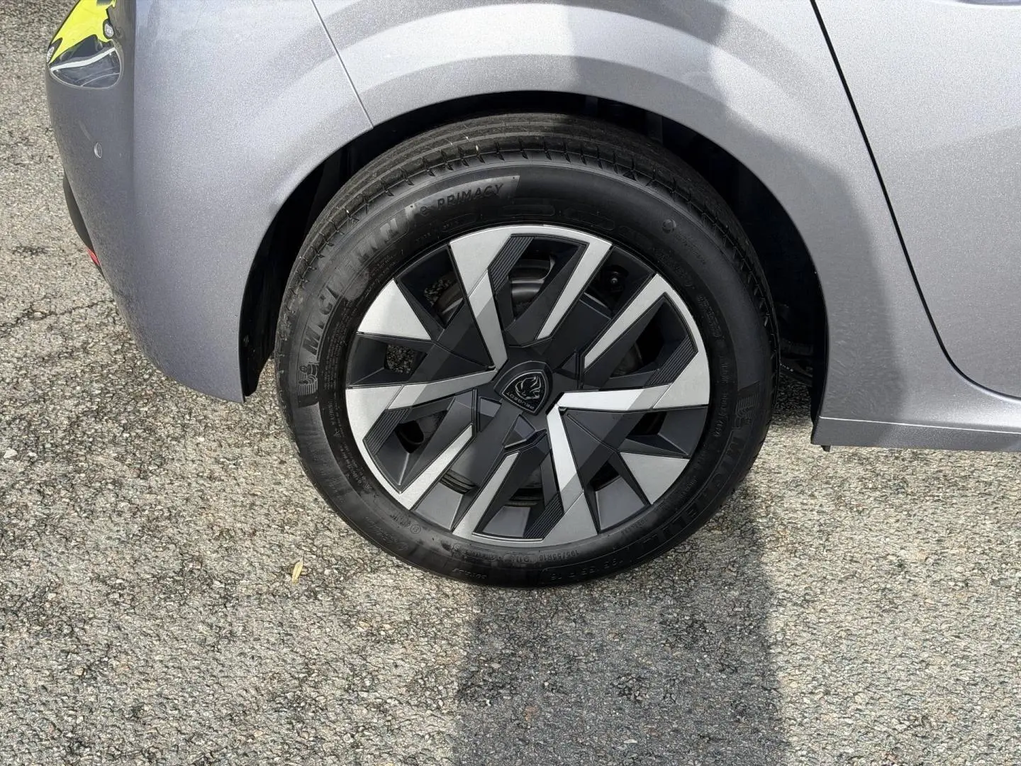 Gros plan sur la roue arrière droite d'une Peugeot 208 1.2 Hybrid gris Artense avec jante au design géométrique noir et argent.