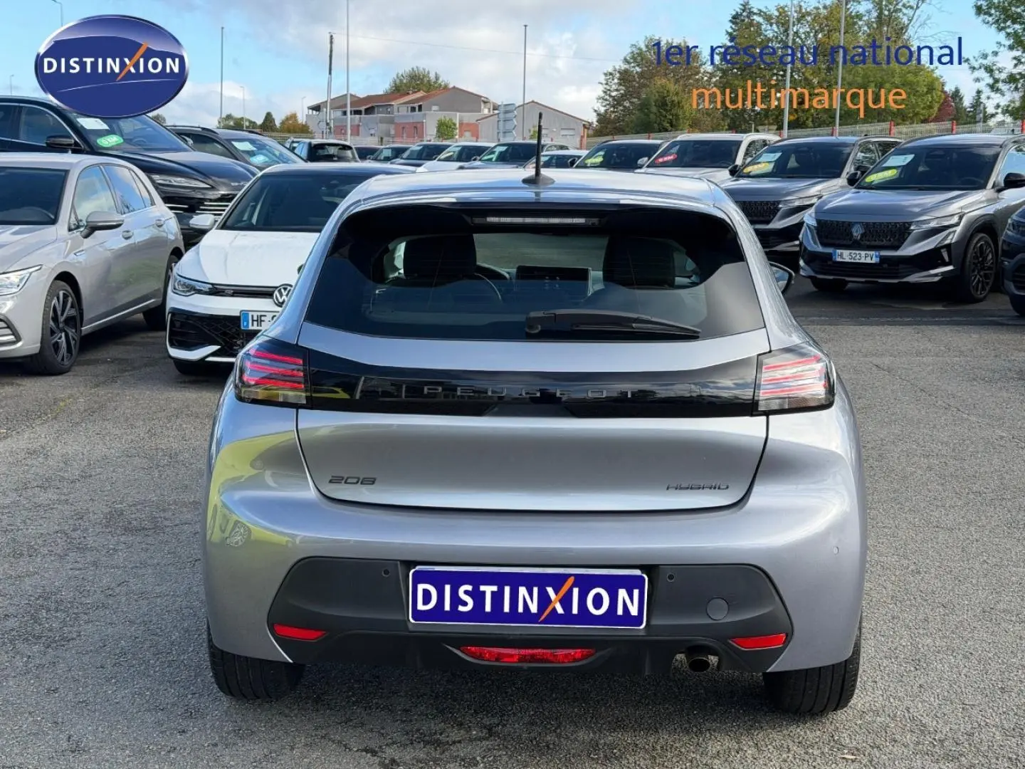 Vue arrière d'une Peugeot 208 hybride gris Artense garée dans un parking multimarque en extérieur.