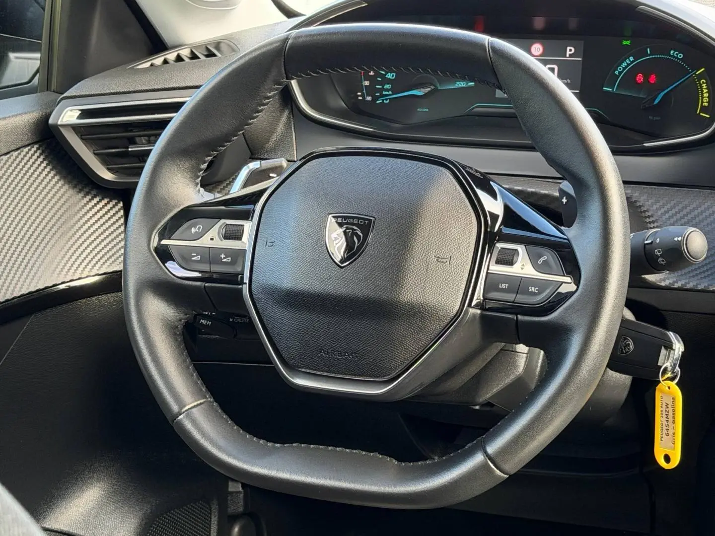 Vue rapprochée du volant noir de la Peugeot 208 1.2 Hybrid 110ch avec tableau de bord numérique en arrière-plan.