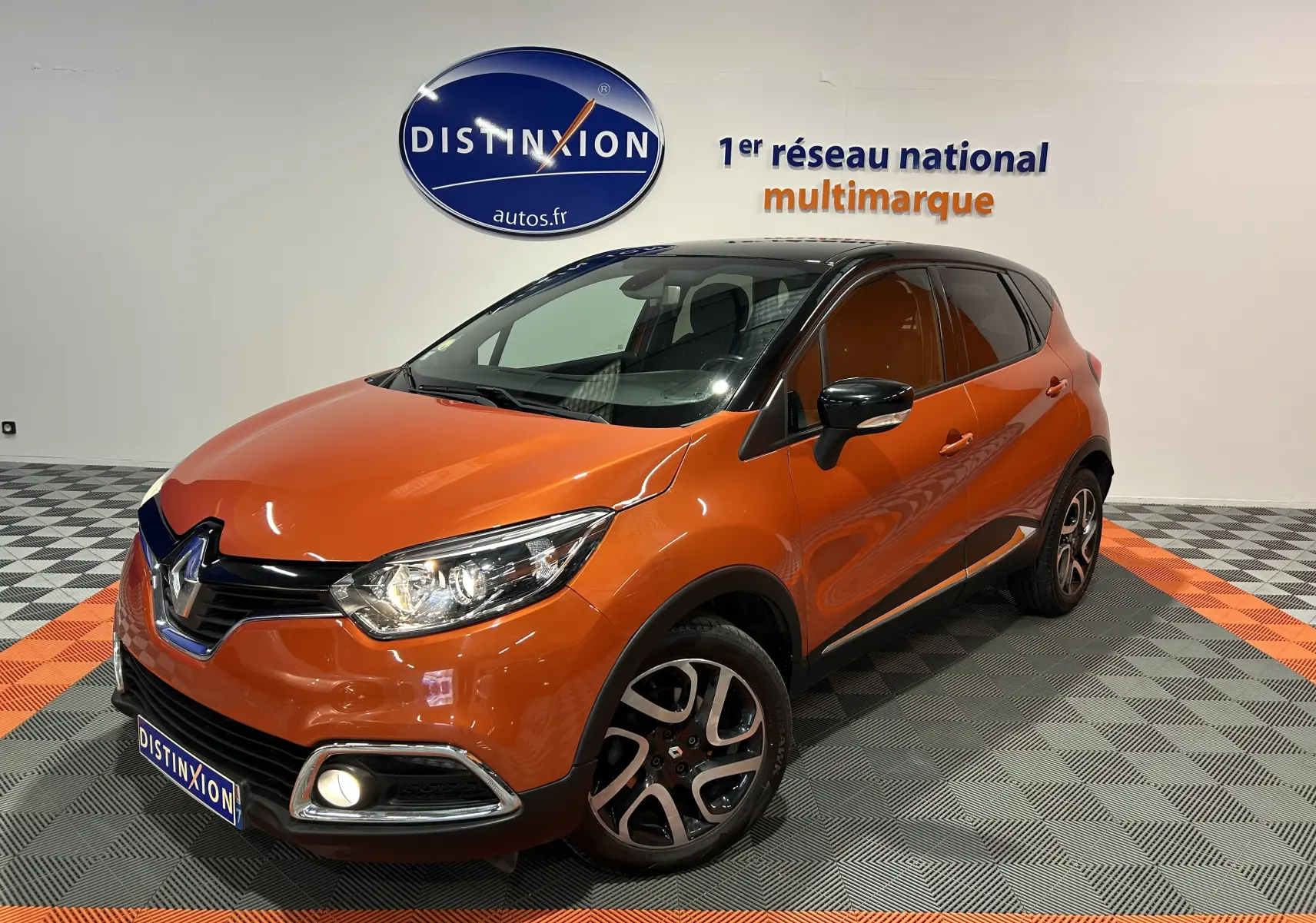 Renault Captur orange vue 3/4 avant droit, toit noir, jantes alliage et phares allumés en showroom.