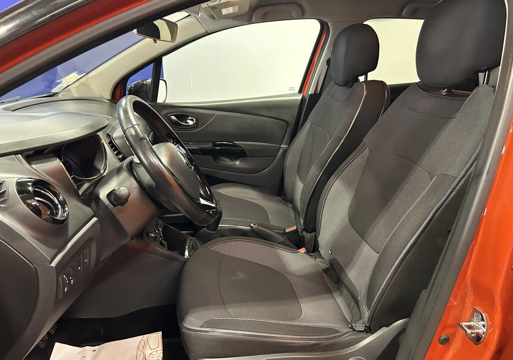 Intérieur avant droit d’un Renault Captur orange 2014, sièges tissu gris et volant multifonction noir.