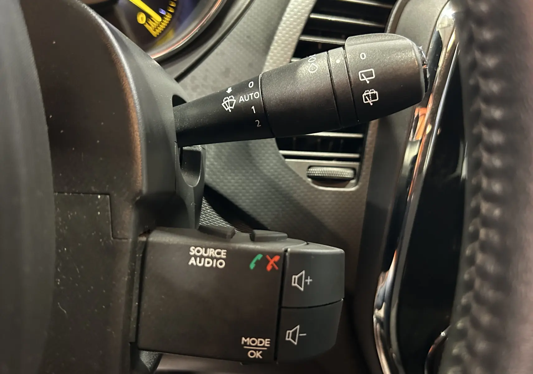 Gros plan sur les commandes au volant côté gauche du Renault Captur orange 2014, avec commandes audio et essuie-glace.