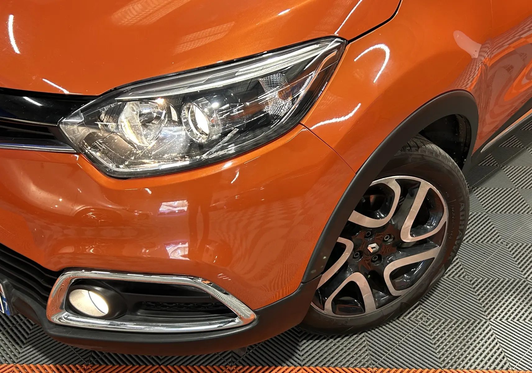 Gros plan sur l'avant droit orange du Renault Captur 2014, mettant en valeur le phare et la roue alliage noire et argent.