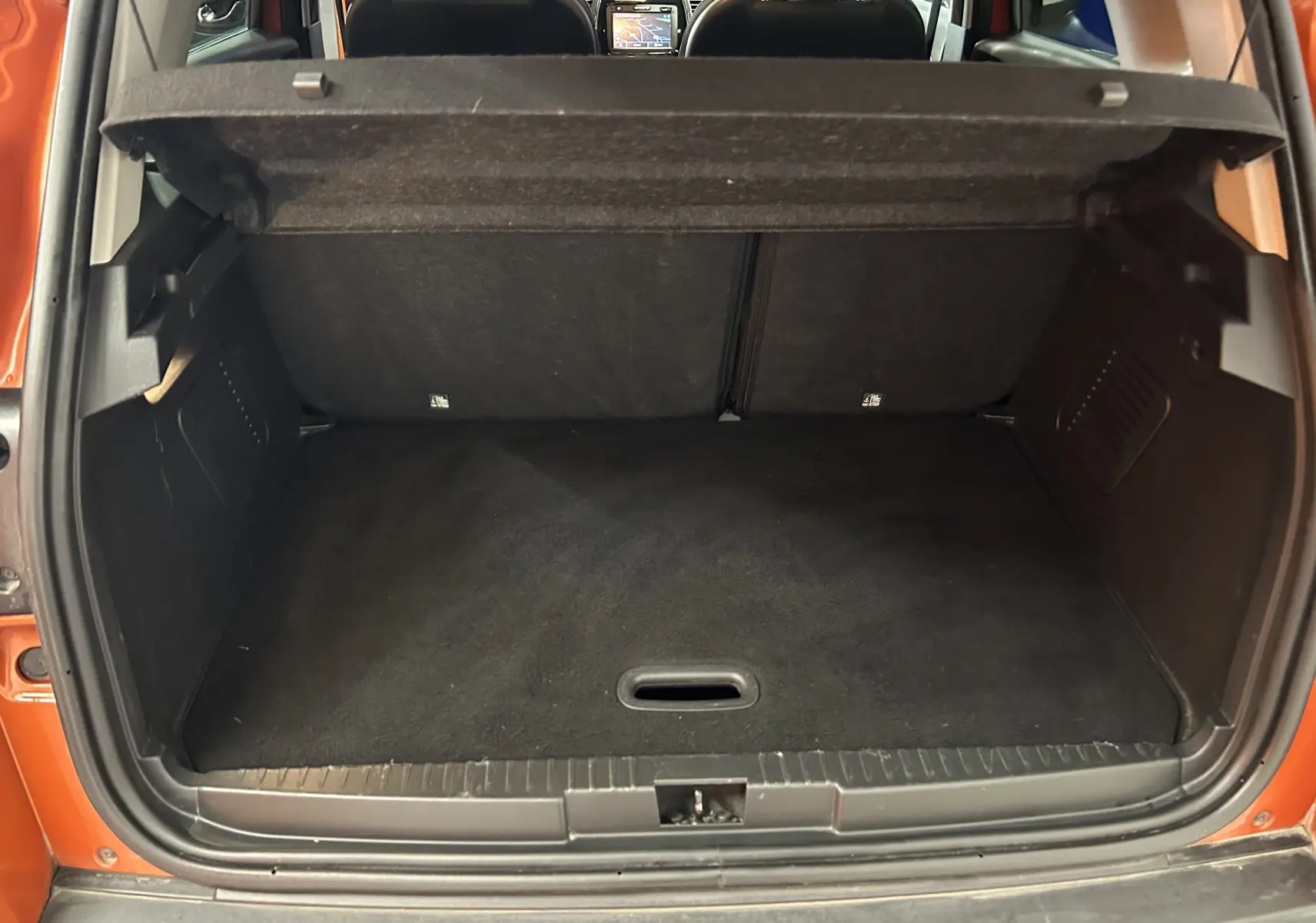 Coffre ouvert vu de l'arrière d'un Renault Captur orange 2014 avec intérieur noir et tablette de séparation relevée.