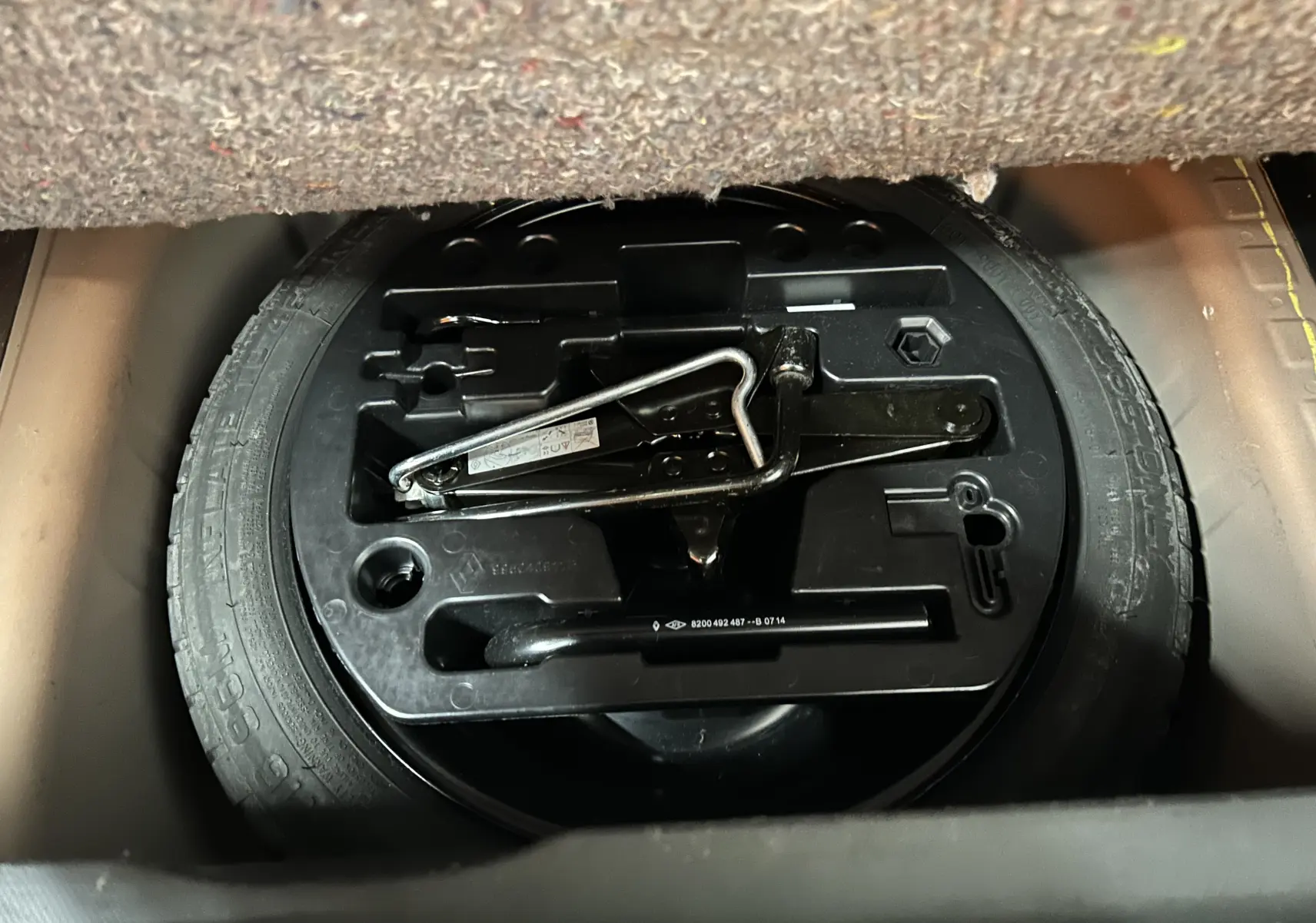 Vue rapprochée de la roue de secours et du cric noir dans le coffre d'un Renault Captur orange de 2014.