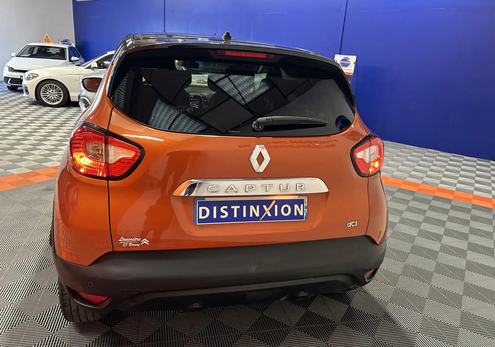 Vue arrière d'un Renault Captur orange diesel de 2014 avec plaque Distinxion dans un showroom.