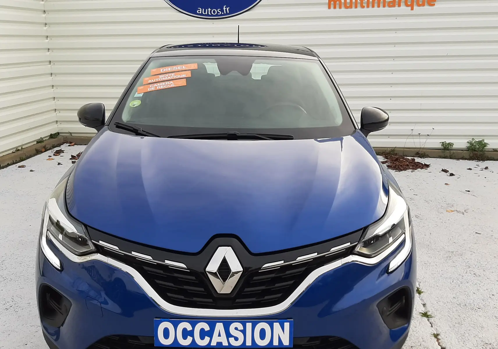 Vue frontale d'un Renault Captur bleu iron avec toit noir, affichant un panneau "OCCASION" sur la calandre.