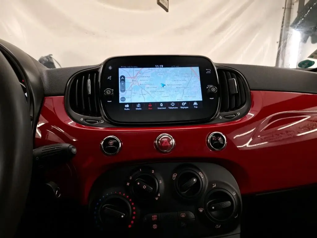 Vue intérieure centrée sur la planche de bord rouge brillante du Fiat 500 Dolcevita avec écran tactile et commandes climatiques.