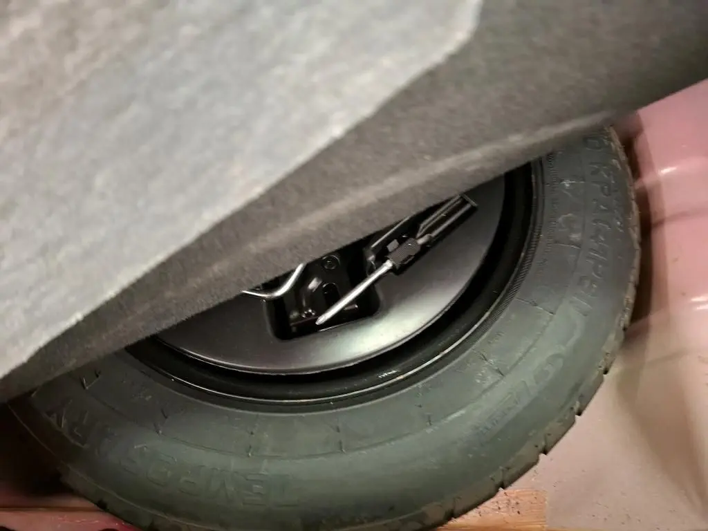 Gros plan sur la roue de secours noire et son outil de levage dans le coffre d'une FIAT 500 rouge Dolcevita 2021.