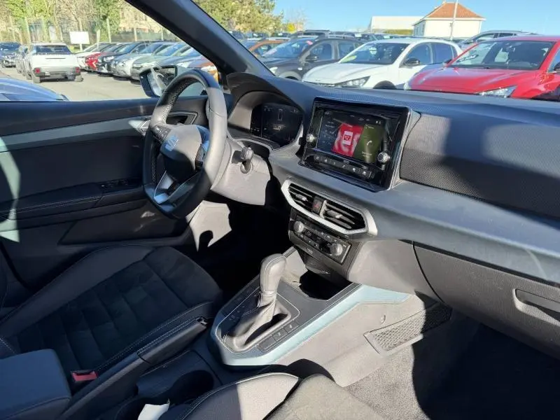 Intérieur du SEAT Arona 2025 vu côté conducteur, montrant le tableau de bord noir avec écran tactile et levier de boîte automatique.