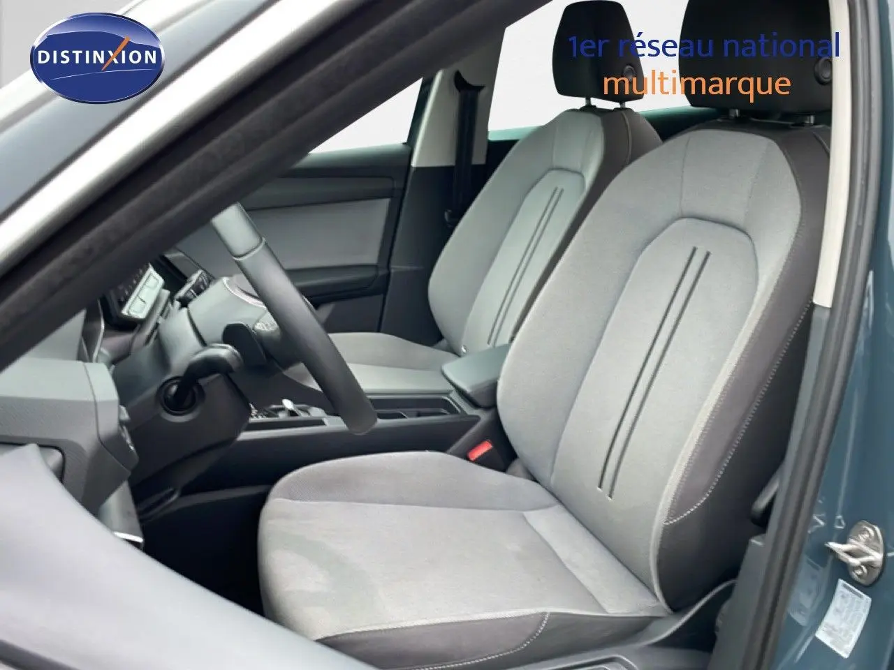 Vue intérieure côté conducteur du SEAT LEON IV 1.5TSI gris Fiord, mettant en valeur les sièges tissu gris clair et la console centrale.