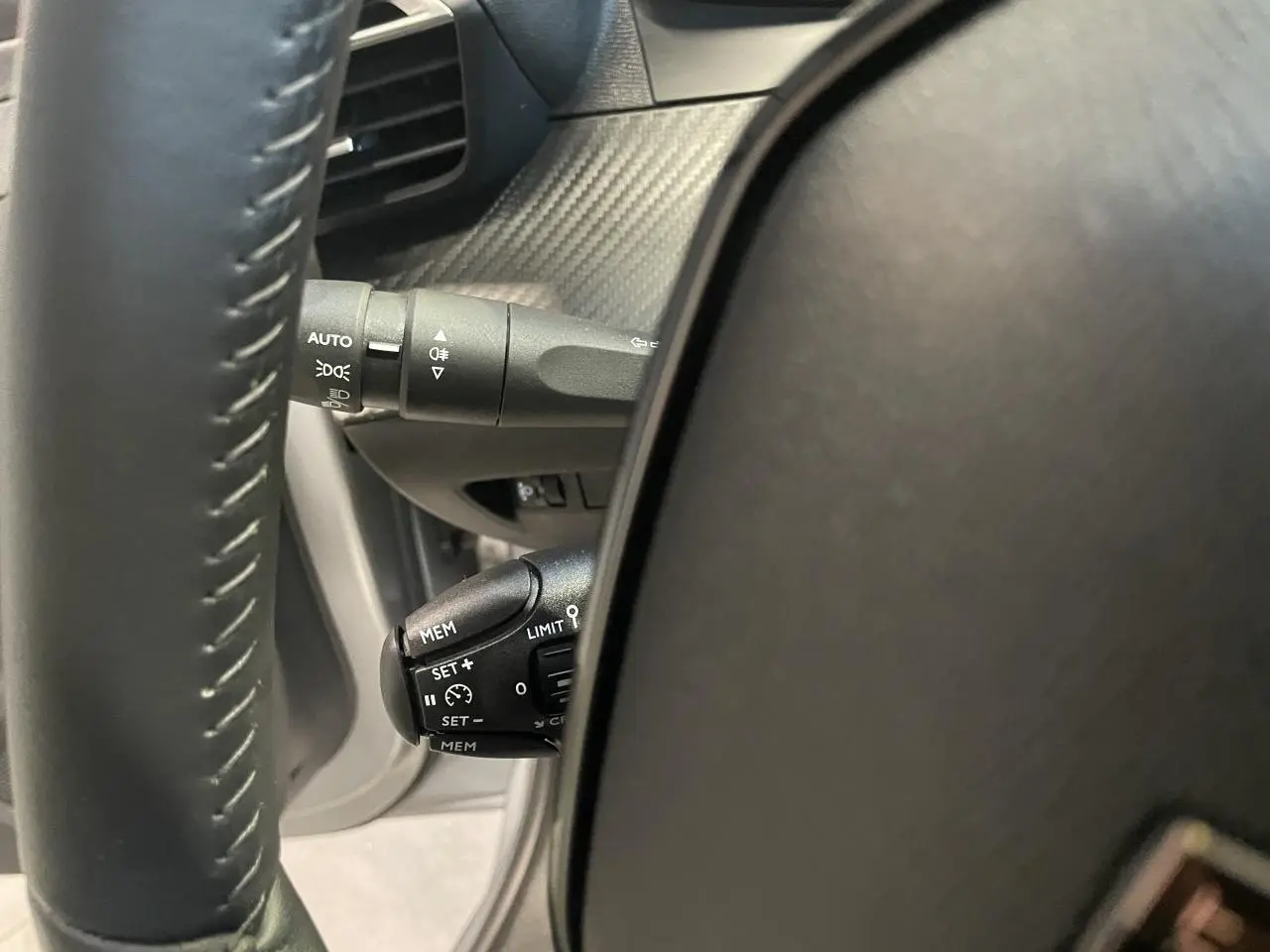 Gros plan sur la commande de régulateur de vitesse à gauche du volant cuir noir du Peugeot 208 gris clair 2024.