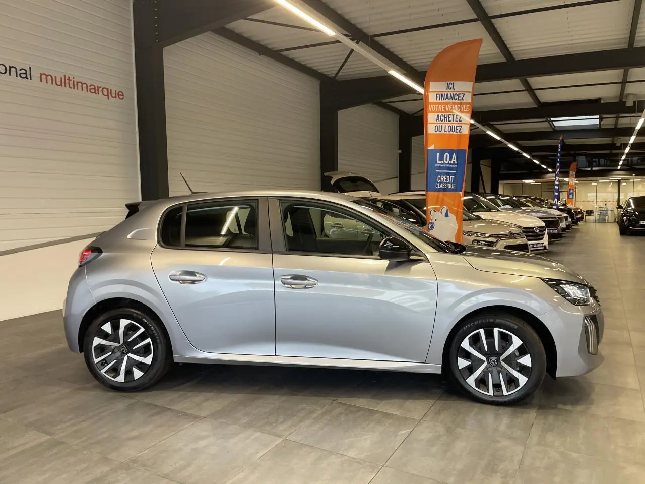 Peugeot 208 gris clair vue de profil côté gauche en intérieur, avec jantes tôle 16'' et rétroviseurs noirs.