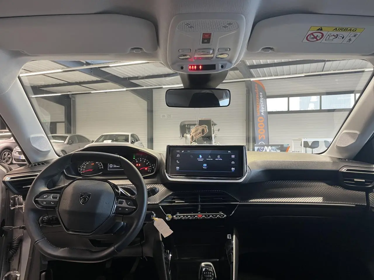 Vue intérieure frontale du tableau de bord noir et volant cuir de la Peugeot 208 1.2i PureTech 2024 avec écran tactile central.