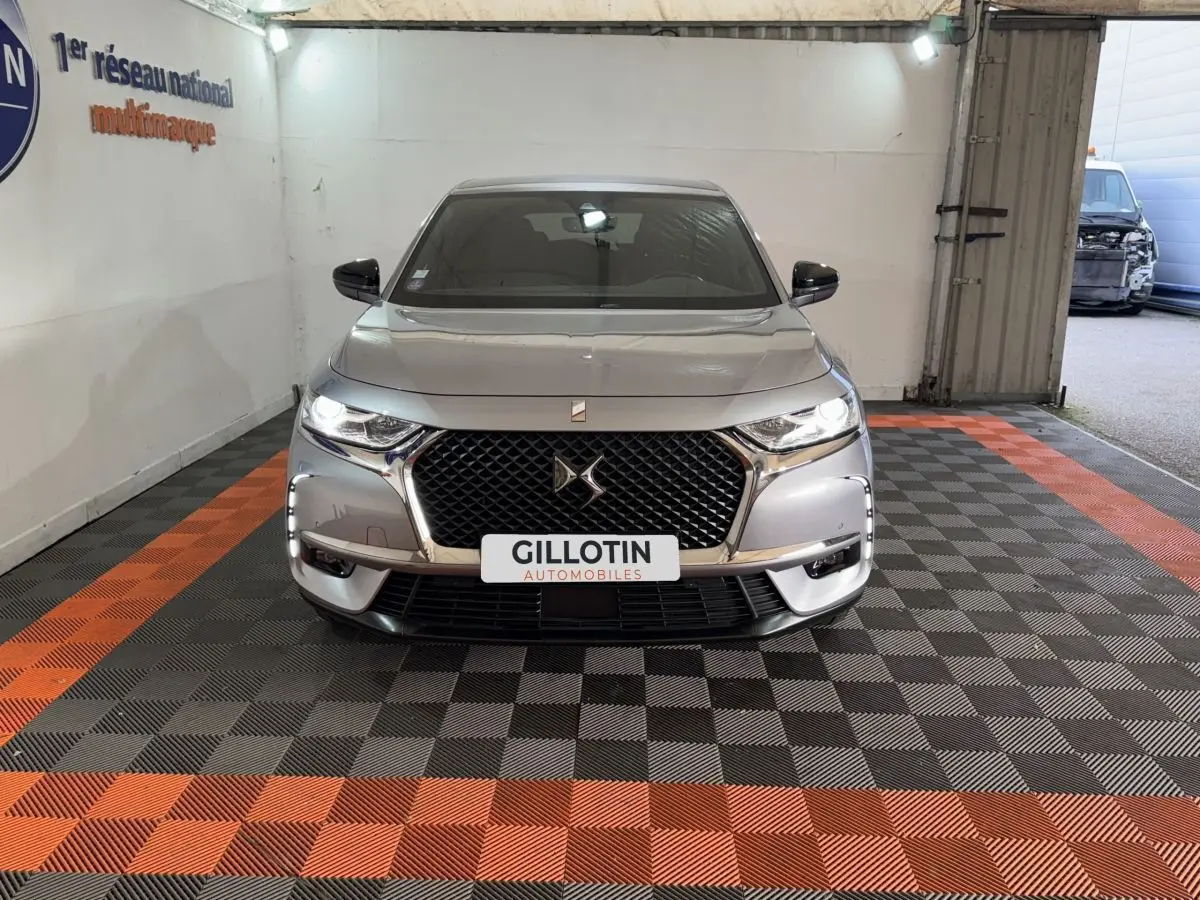 Vue frontale d’un DS7 Crossback gris foncé avec calandre noire à motif losange et phares LED allumés, en intérieur.