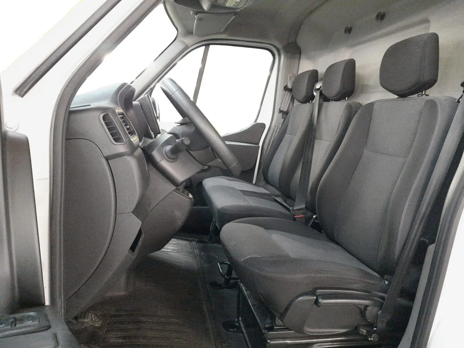 Vue intérieure côté conducteur du Renault Master L1H1 2023 blanc, montrant les trois sièges en tissu gris et le tableau de bord.