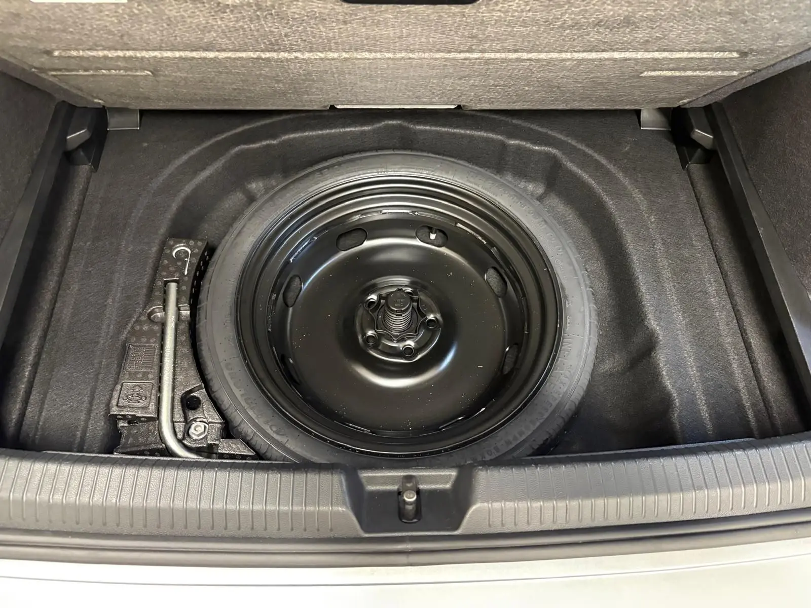 Vue plongeante sur la roue de secours noire dans le coffre d'une Volkswagen Golf 2.0 TDI 2025 couleur reflet d'argent.