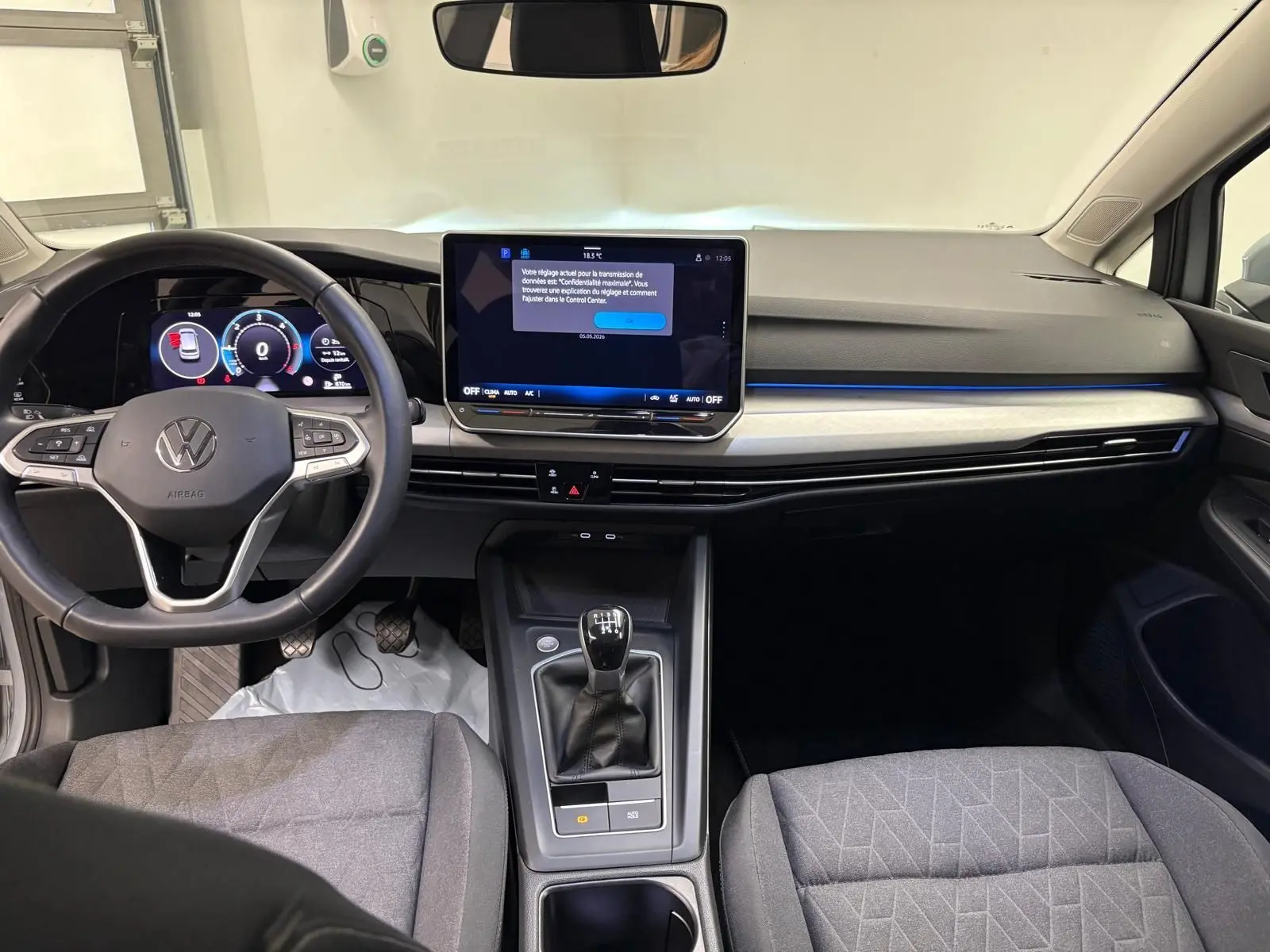 Intérieur de Volkswagen Golf 2025 en vue frontale, tableau de bord noir avec écran tactile et levier de vitesse manuel.
