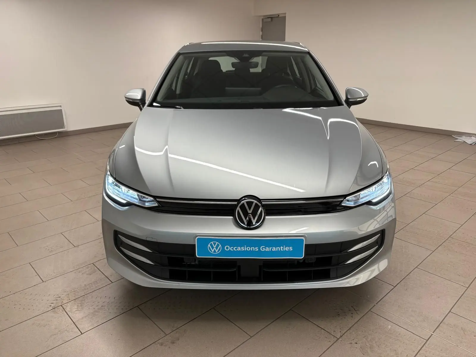 Vue frontale d'une Volkswagen Golf 2.0 TDI 116 BVM6 Life Plus 2025 en reflet d'argent avec phares allumés.