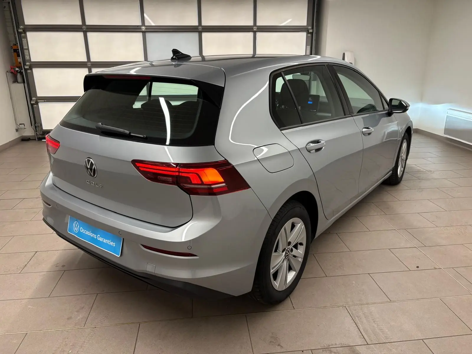 Vue 3/4 arrière droite d'une Volkswagen Golf 2.0 TDI 2025 couleur reflet d'argent avec feux arrière allumés en intérieur.