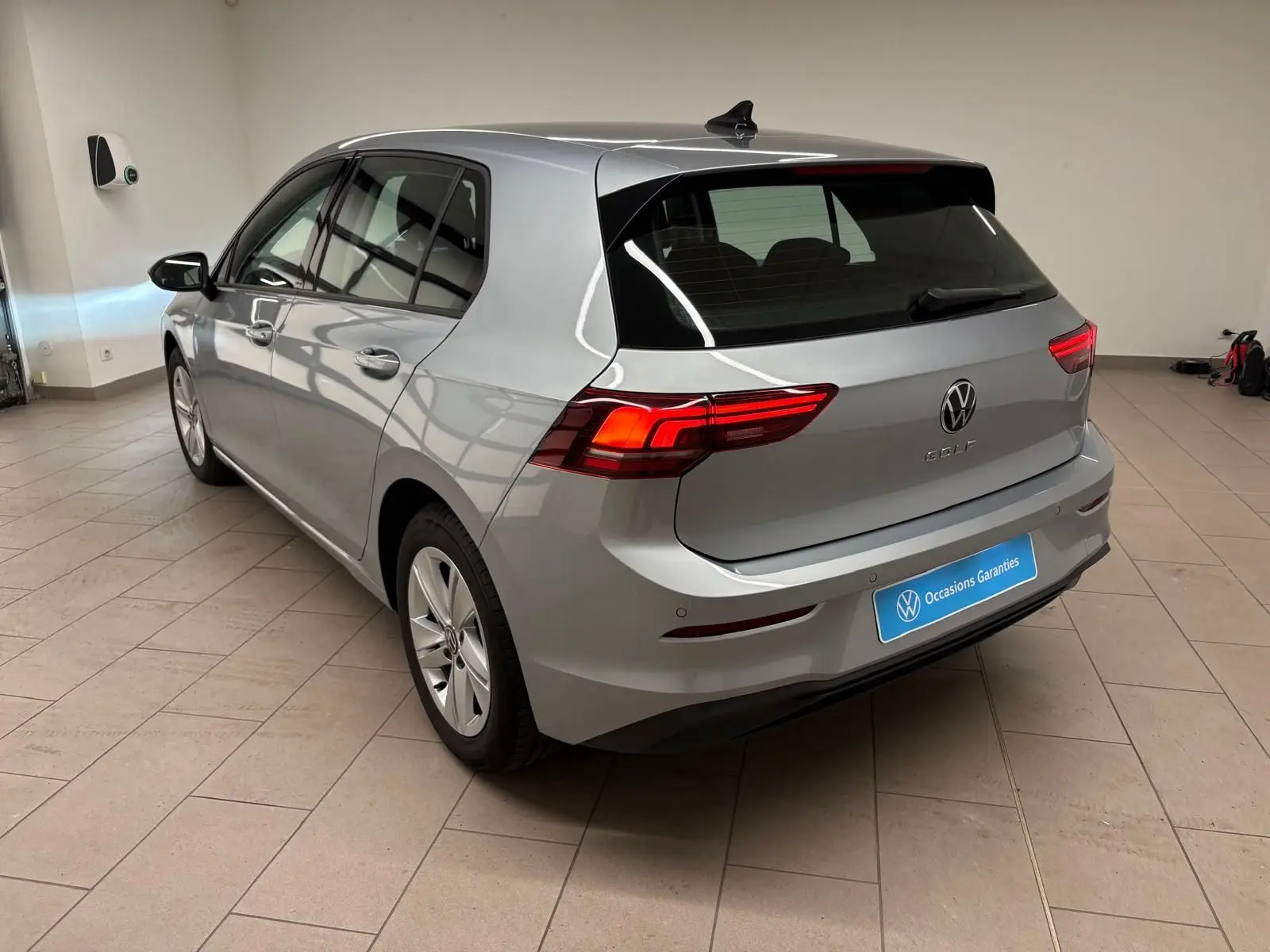 Vue 3/4 arrière droite d'une Volkswagen Golf 2025 argent reflet, avec feux arrière allumés dans un showroom.
