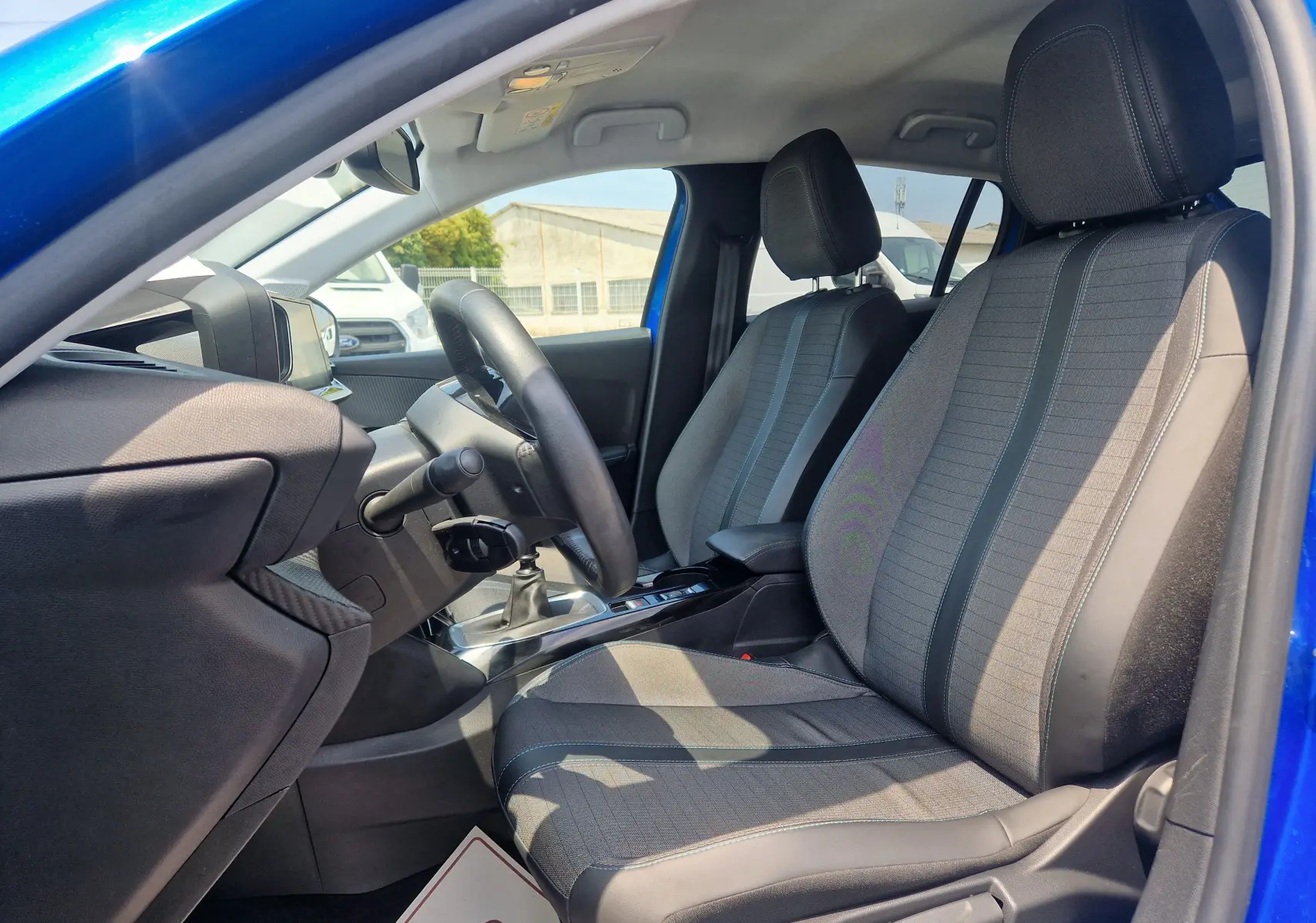 Vue intérieure côté conducteur de la Peugeot 208 bleu Vertigo 2022, montrant les sièges tissu et cuir et le volant.