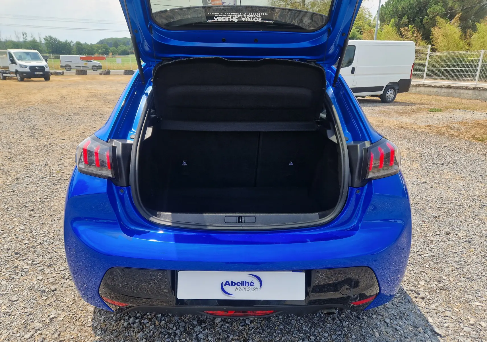 Vue arrière d'une Peugeot 208 bleu Vertigo 2022 avec coffre ouvert, mettant en valeur les feux arrière à griffes rouges.